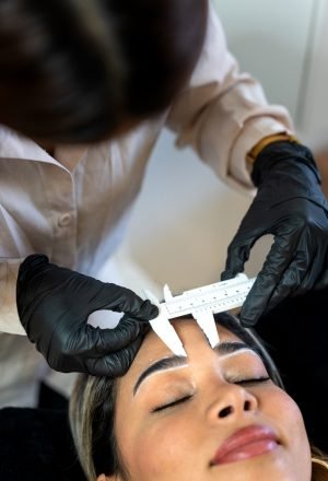 Professional Latin esthetician measuring a client's eyebrows for her treatments.